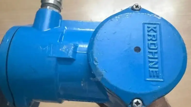 Close-up of a scuffed blue industrial device with a round bolted metal cover on a wooden tabletop