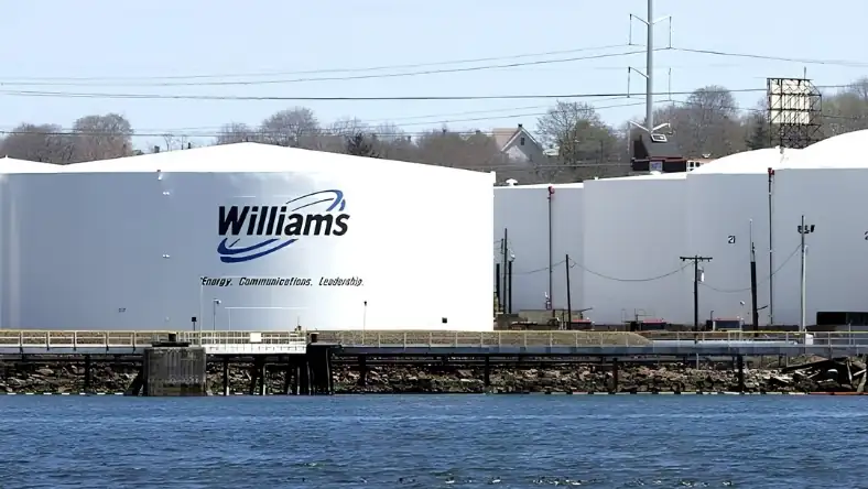 Row of large white storage tanks beside a wooden dock, with power lines and a clear blue sky above