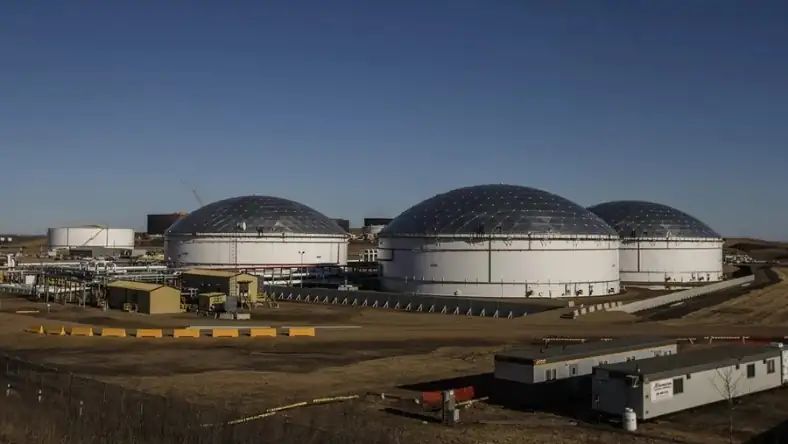 Three large domed storage tanks sit at an industrial site with smaller buildings and equipment nearby