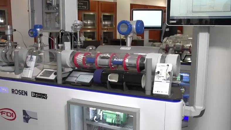 Industrial pipeline monitoring equipment with blue sensors and clear pipe sections on an exhibition stand